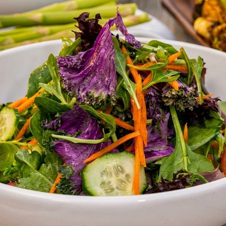 A vibrant garden salad with mixed greens, purple kale, carrots, cucumbers, and tomatoes in a white bowl.