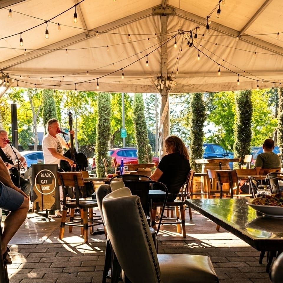 Patrons enjoy live music under a string-lit tent at an outdoor restaurant patio.