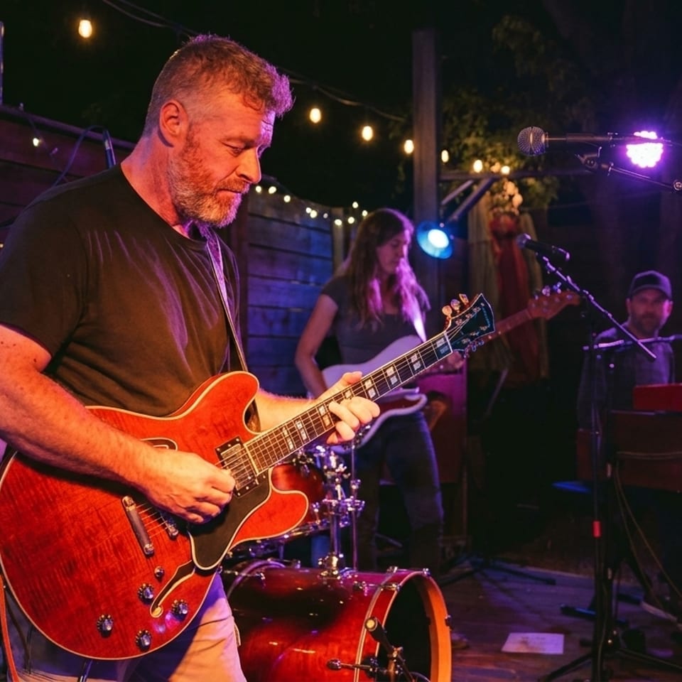 A band performs live on an outdoor stage, illuminated by purple and string lights.